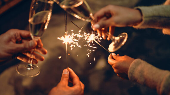 Happy New Year and Merry Christmas! Glasses with champagne in hand and sparklers.