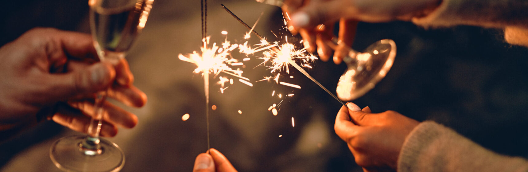 Happy New Year and Merry Christmas! Glasses with champagne in hand and sparklers.