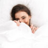 Photo from above of cute woman 20s smiling while lying in bed on white pillow after sleep or nap