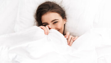 Photo from above of cute woman 20s smiling while lying in bed on white pillow after sleep or nap
